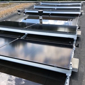 De afbeelding toont zonnepanelen die op een plat dak zijn geïnstalleerd, met reflectie van de lucht op de panelen en water op het dak.