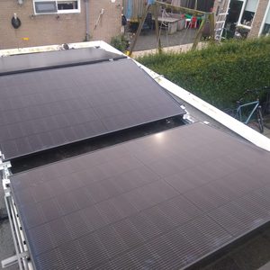 Installatie van zonnepanelen op een dak, met een technicus die de panelen aanbrengt. De zonnepanelen zijn zwart en goed zichtbaar in de foto.