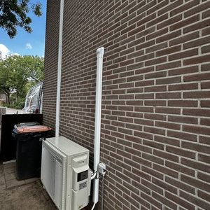 Een wandairconditioner met een buitenunit, geïnstalleerd op de gevel van een gebouw. Verbindingsbuizen zijn zichtbaar voor koelsysteem.