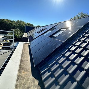 De afbeelding toont een installatie van zonnepanelen op een hellend dak, met een heldere lucht op de achtergrond.