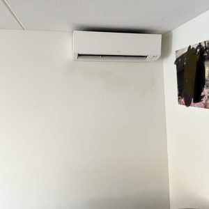 De afbeelding toont een binnen-unit van een airconditioning installatie, bevestigd aan de muur en een plafond met verlichting.