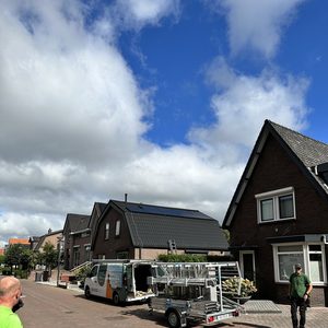 De foto toont een zonnepanelen installatieproject in een woonwijk, met zonnepanelen op het dak van een huis en installateurs die materialen voorbereiden.