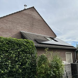 Een woning met zonnepanelen op het dak, omringd door weelderige begroeiing.