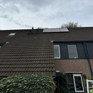 De afbeelding toont zonnepanelen die op een hellend dak zijn geïnstalleerd, met een beschutte omgeving door de omliggende begroeiing.