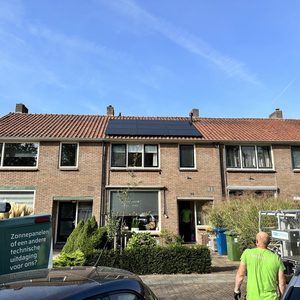 Een woning met zonnepanelen op het dak, wat duidt op een zonne-energie installatie. De installatie is zichtbaar met enkele mensen die aan het werk zijn op de locatie.