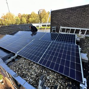 Een installatie van zonnepanelen op een hellend dak, met een technicus die de panelen monteert.