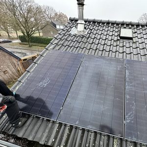 De afbeelding toont zonnepanelen die op een hellend dak zijn geïnstalleerd. Een installateur is zichtbaar bezig met de montage.