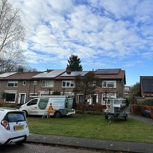 De afbeelding toont een installatie van zonnepanelen op meerdere daken, met een van een installatievoertuig en een persoon in de buurt.