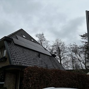Een installatie van zonnepanelen op een schuin dak van een woning, zichtbaar met een grijze lucht op de achtergrond.