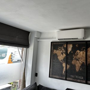 De afbeelding toont een opgehangen airco-installatie in een woonkamer, met een wereldkaart aan de muur.