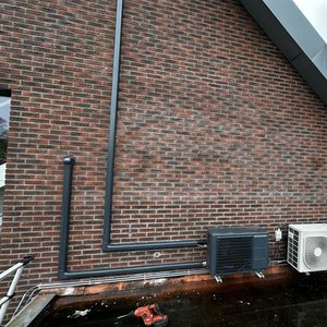 De afbeelding toont een buitenunit van een airconditioning installatie, inclusief leidingen en bevestiging aan de muur.