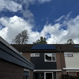 De foto toont een woning met zonnepanelen op het dak, onder een heldere lucht met enkele wolken.