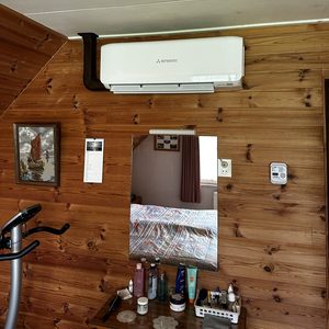 Een wandgemonteerde airconditioningseenheid geïnstalleerd aan de muur in een houten omgeving, met zicht op een spiegel en een fitnessapparaat.