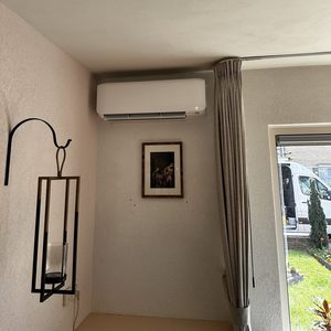 Een airconditioningseenheid is geïnstalleerd aan de muur in een woonruimte, met een decoratieve lamp en een schilderij in de omgeving.