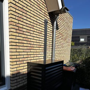 De afbeelding toont een externe airco-unit net naast een stenen muur, goed geïnstalleerd en verbonden met de muur.