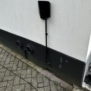 Een laadpaal voor elektrisch voertuigen, wandgemonteerd aan een muur, met bekabeling en ventilatieopeningen zichtbaar.