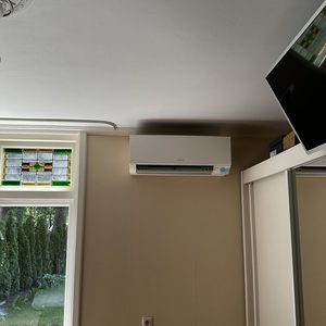 Een wand-geïnstalleerde airconditioningseenheid in een ruimte met een raam en een moderne uitstraling.
