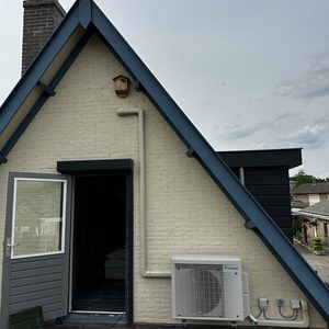 De foto toont een externe airconditioningsunit van het merk Daikin, geïnstalleerd aan de buitenmuur van een huis.