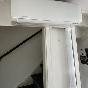 Een geïnstalleerde airconditioner aan de muur met zichtbare leidingen en een nabijgelegen trap.