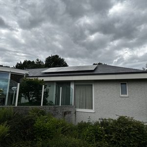 De foto toont zonnepanelen die op de dakrand van een woning zijn geïnstalleerd, omgeven door groene begroeiing.