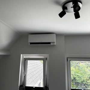 Een wandgemonteerde airconditioner in een kamer met twee ramen, biedt koeling en comfort.