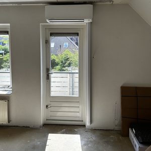De foto toont een recent geïnstalleerde airconditioningseenheid aan de muur in een kamer, met een zicht op de buitenomgeving.