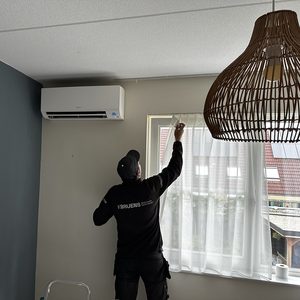 Een airco-installatie wordt geïnstalleerd in een woonkamer, met aandacht voor de plaatsing en afwerking.