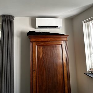 De afbeelding toont een wand-airco-installatie boven een kast in een lichte kamer.