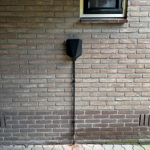 Een laadpaal voor elektrische voertuigen, bevestigd aan een bakstenen muur, met een eenvoudige en functionele uitstraling.