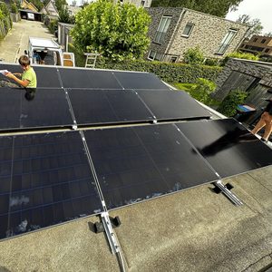 De afbeelding toont een installatie van zonnepanelen op een dak, met een technicus die bezig is met de montage.