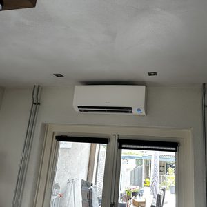 Een wandmodel airconditioningunit is geïnstalleerd aan het plafond, met zichtbare leidingen die aan de wand zijn bevestigd.