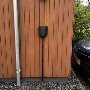 De afbeelding toont een laadpaal voor elektrische voertuigen, netjes gemonteerd aan een houten wand met een aangesloten kabel.