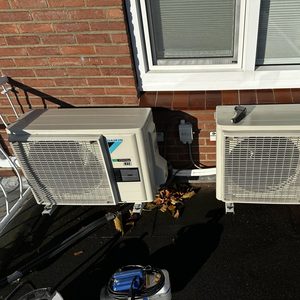 De afbeelding toont een buitenunit van een airconditioningsysteem, gemonteerd op een betonnen oppervlak met aansluitingen naar binnen.