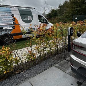 De afbeelding toont een laadpaal voor elektrische voertuigen, geïnstalleerd in een rustige omgeving met een bedrijfswagen op de achtergrond.