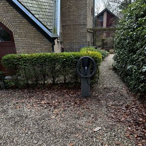 Een laadpaal voor het opladen van elektrische voertuigen, geplaatst in een oprit omgeven door groen