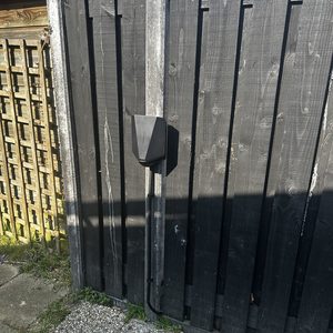 Een laadpaal is geïnstalleerd aan een houten schutting, klaar voor het opladen van elektrische voertuigen.