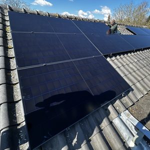 Een installatie van zonnepanelen op een hellend dak, zichtbaar zijn meerdere zonnepanelen en een installateur bezig met de montage.
