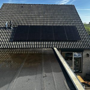 Een installatie van zonnepanelen op een hellend dak met een blauwe lucht op de achtergrond.
