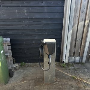 Dit is een laadpaal voor elektrische voertuigen, bevestigd aan een betonnen paal in een externe omgeving.