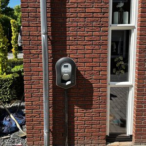 Een laadpaal voor elektrische voertuigen, bevestigd aan een bakstenen muur, met een elektronische interface voor opladen.
