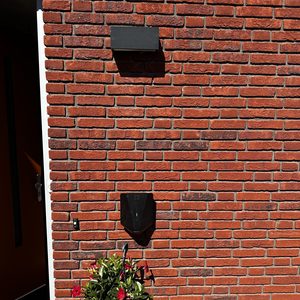 Een laadpaal voor elektrische voertuigen is geïnstalleerd aan de muur, naast een bloempot met bloemen.