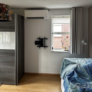 De afbeelding toont een geïnstalleerde airconditioningseenheid aan de muur, in een slaapkamer met een ontspannen inrichting.