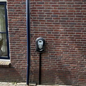 De afbeelding toont een laadpaal voor elektrische voertuigen aan een bakstenen muur.