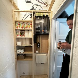 De afbeelding toont een nog niet volledig afgemaakte meterkast met enkele elektrische componenten en opslagruimtes voor materialen.