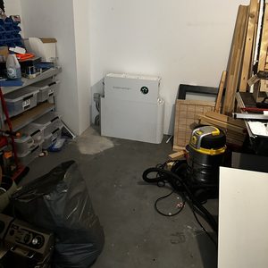 Installatie van een thuisbatterij in een garage, met diverse benodigdheden en opslag in de omgeving.