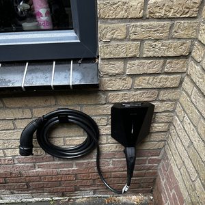 Een laadpaal voor elektrische voertuigen is geïnstalleerd aan de muur, compleet met een oplaadkabel.