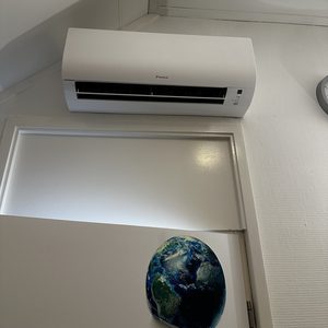 Een wandunit van Daikin voor airconditioning, geïnstalleerd in een kamer met een deur op de achtergrond.