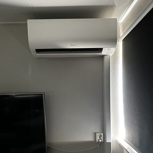 Moderne wandunit airconditioning geïnstalleerd in een woonkamer, met een zichtbare voedingskabel en dichtbij een televisie.