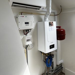 De afbeelding toont een airconditioningseenheid gemonteerd aan de muur, samen met bijbehorende leidingen en een meterkast.