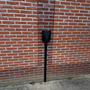 Een laadpaal voor elektrische voertuigen is geïnstalleerd tegen een bakstenen muur, zichtbaar met aansluitingen.